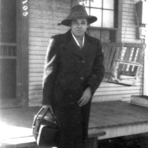 African-American woman in hat and suit with a bag in front of house with front porch swing