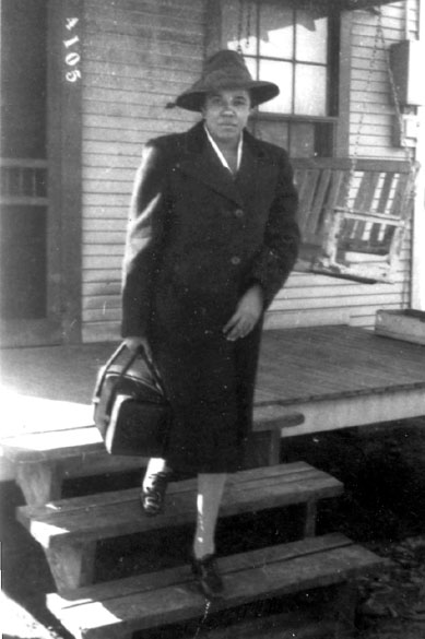 African-American woman in hat and suit with a bag in front of house with front porch swing