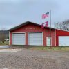 Red metal building with three garage bay doors and flagpoles