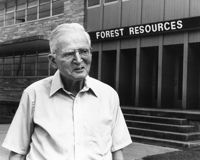 Older white man in glasses outside wood and brick building