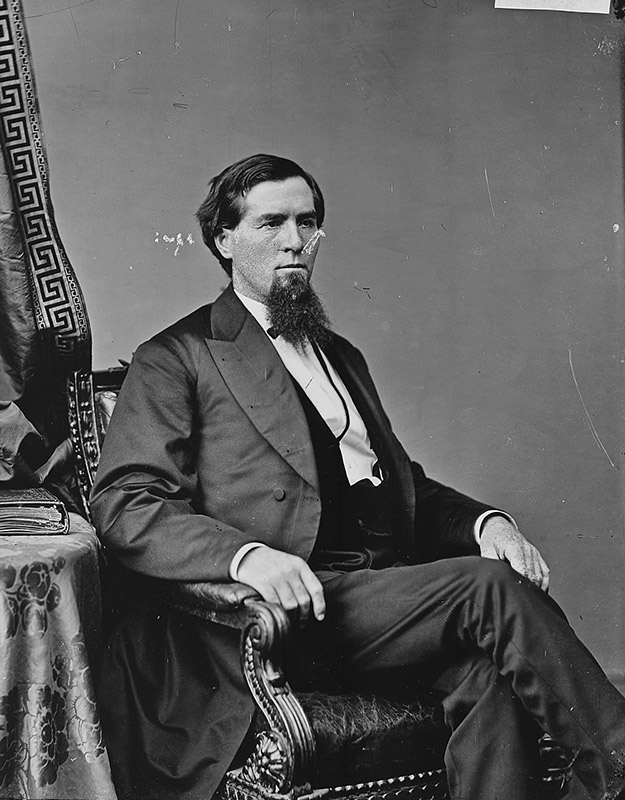 White man with beard in formal attire seated in chair