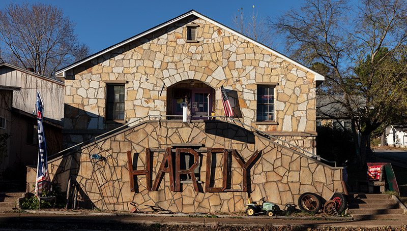 Single-story stone house with "Hardy" sign on double staircase in the foreground