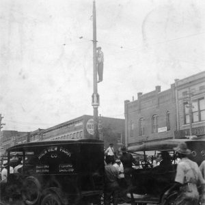 African-American man hanging from telephone pole surrounded by town buildings and cars