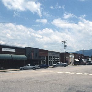 storefronts on street with corner building with curved green awnings with power lines and mountain in the background