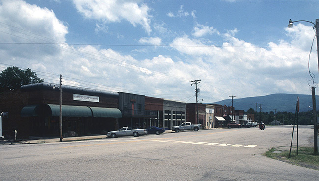 storefronts on street with corner building with curved green awnings with power lines and mountain in the background