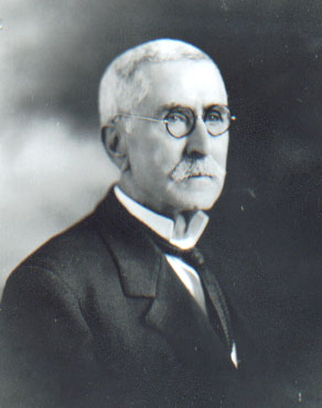 Older white man with round glasses in suit and tie