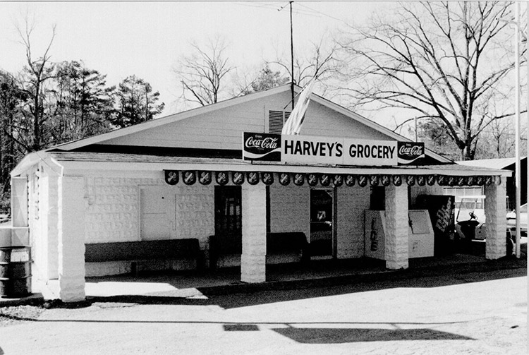 Single-story storefront "Harvey's Grocery" with ice cooler and dr. pepper machine