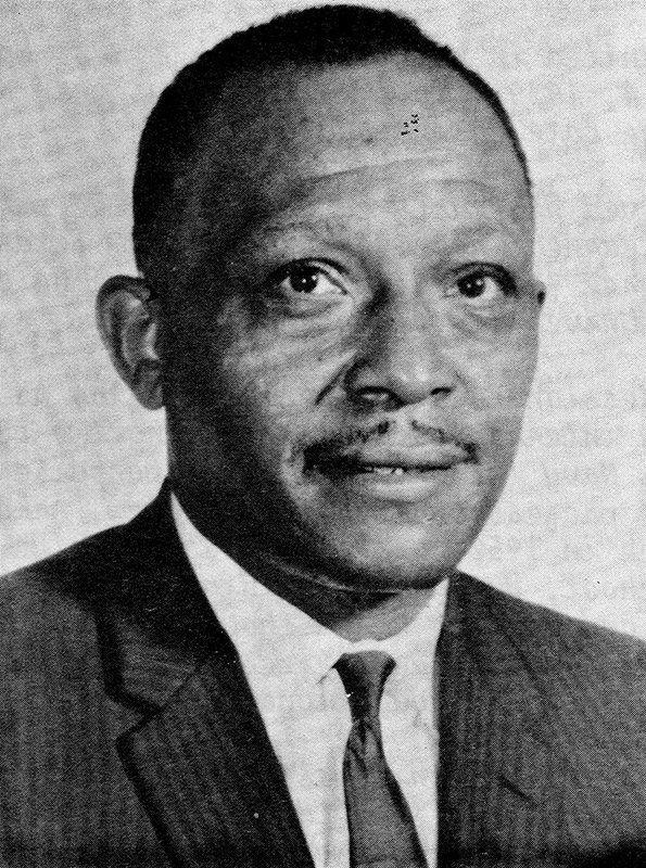 African-American man with mustache smiling in suit and tie