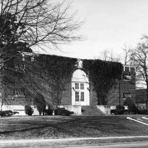 rectangular brick gymnasium building with ivy on front and arched entrance
