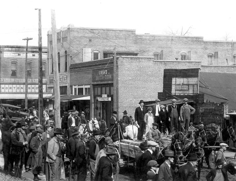 Crowded street with brick buildings and horse drawn wagon