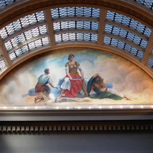 Glass roof with marble supports above a painting of a woman in armor holding sword and two white men in robes on either side of her