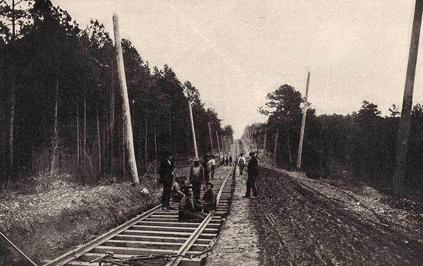Men on railroad tracks with trees on both sides of the tracks