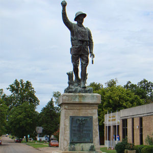 Statue of soldier with his left hand raised on stone pedestal with plaque