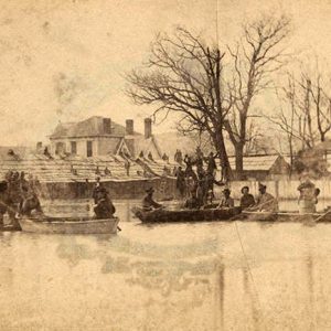 Men in boats on flooded street with houses in the background