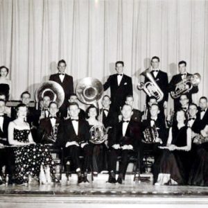 Group of young white men and women with musical instruments posing on stage