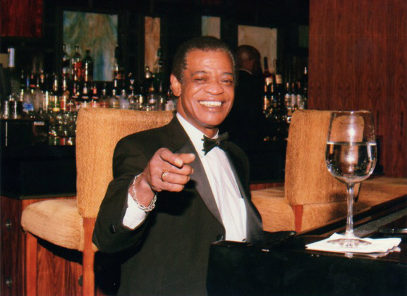 African American man in suit and bow tie sitting in bar pointing at camera