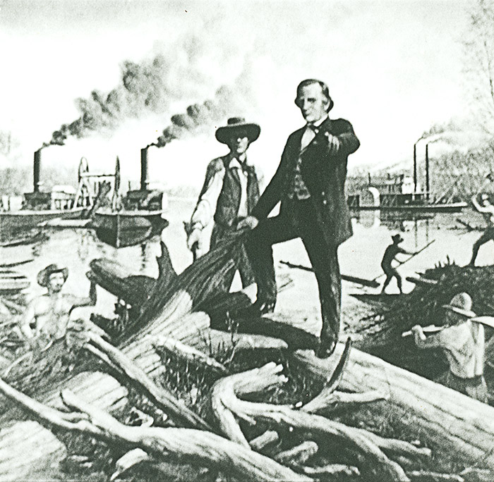 White man with hat and vest standing amid uprooted tree trunks next to another white man in suit with steamboats behind them