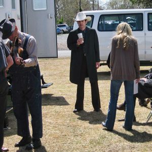 White actors in costume and white woman with trailers and van on film set