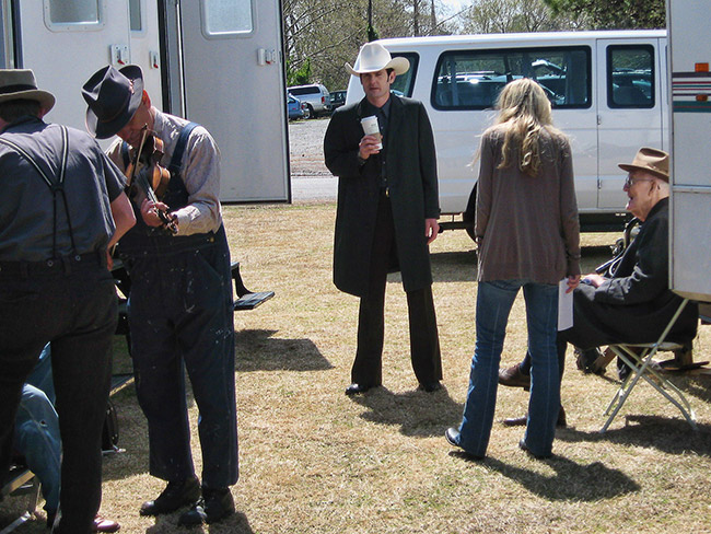 White actors in costume and white woman with trailers and van on film set