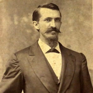 White man with mustache and beard standing in suit