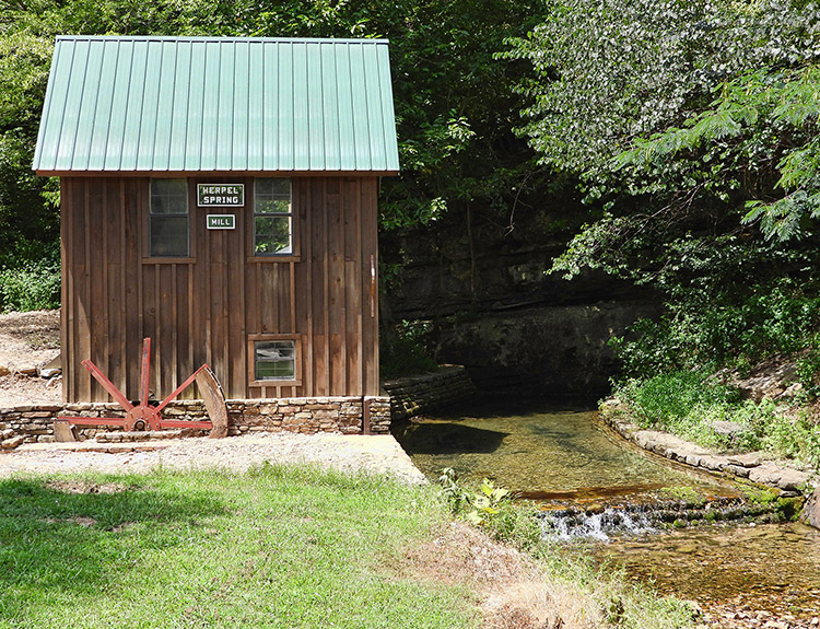 Small mill building with green metal roof and running stream