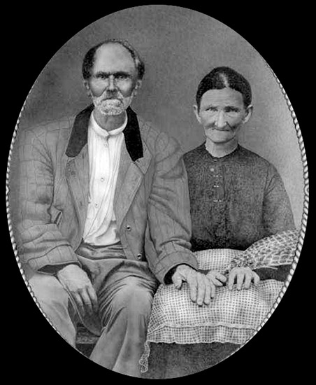 Old white man with beard sitting next to old white woman in dress in oval frame