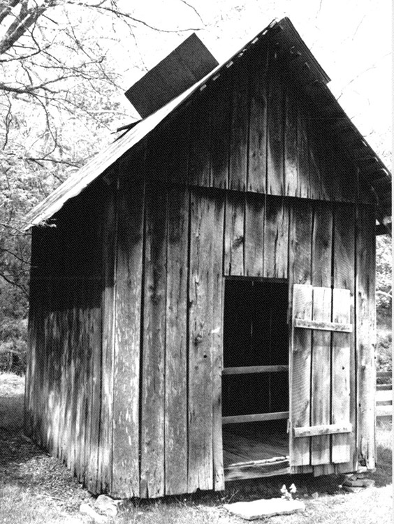Narrow wooden outbuilding with two slats blocking door opening