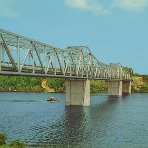 Small boat passing under steel truss bridge on river