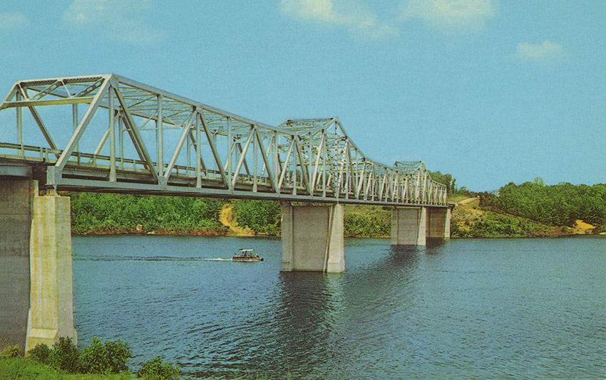 Small boat passing under steel truss bridge on river