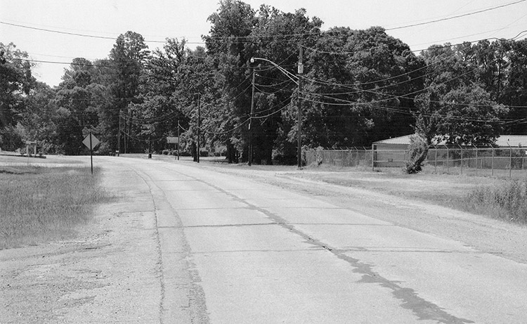 Highway section with fenced-in building on the right and power lines and trees