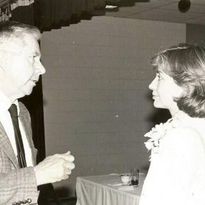 Young white woman speaking to older white man in suit and tie