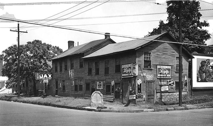 Two-story building with signs and historical marker on street corner