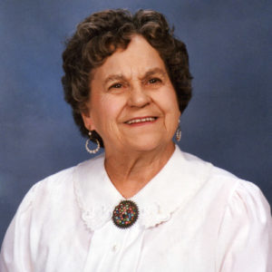 Older white woman in white dress with brooch and loop earrings