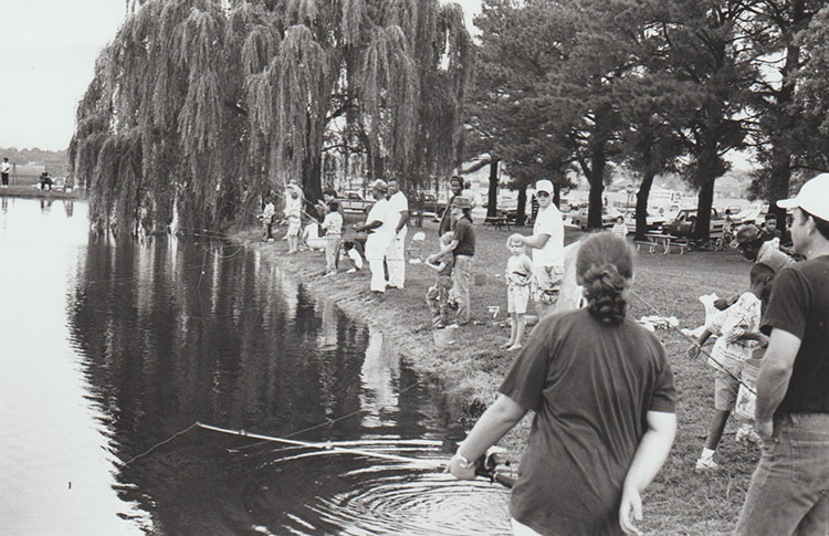 Mixed group of men women and children fishing in hatchery pond with willow trees in the background