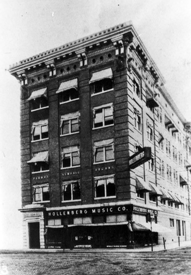 multistory building on street corner with sign saying "Hollenberg Music Co." on first floor
