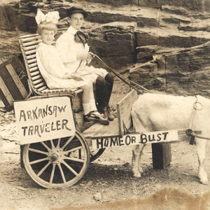 White boy and girl smiling on "Arkansas Traveler Home or Bust" tied to goat