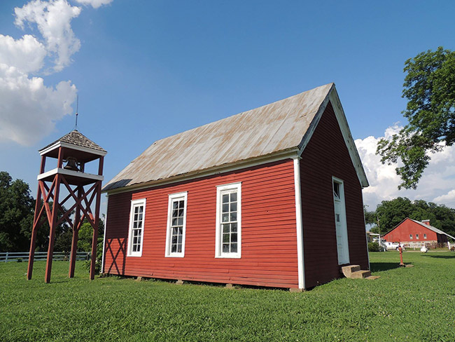 Bell tower next to single-story building painted red with open gable roof on grass