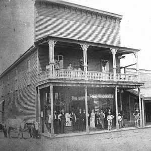 White patrons standing on covered porch and balcony of multistory hotel building on dirt road