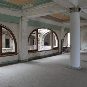 Interior of abandoned hotel ballroom with arched windows and columns
