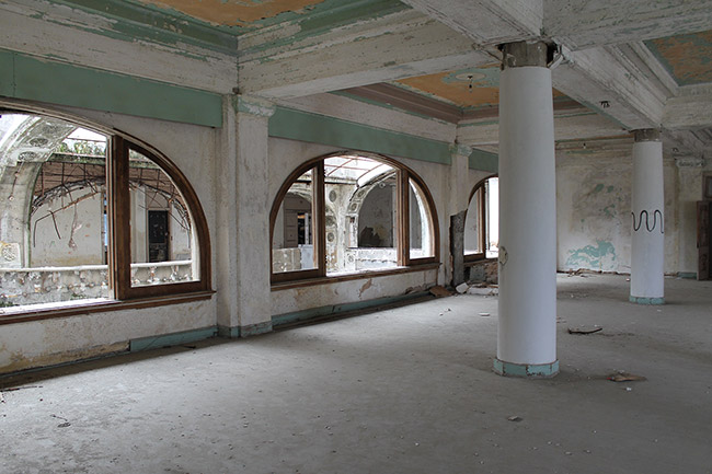 Interior of abandoned hotel ballroom with arched windows and columns