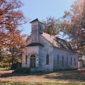 Single-story building with chipped white paint and arched windows and bell tower