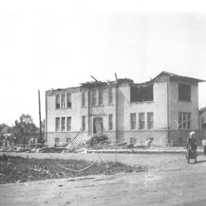 Damaged multistory building with debris and people and car