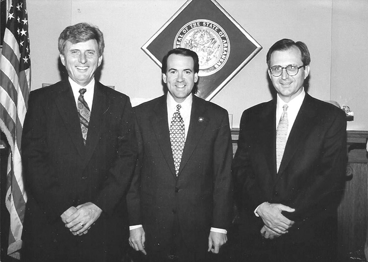 Three white men in suits with state seal and flag behind them
