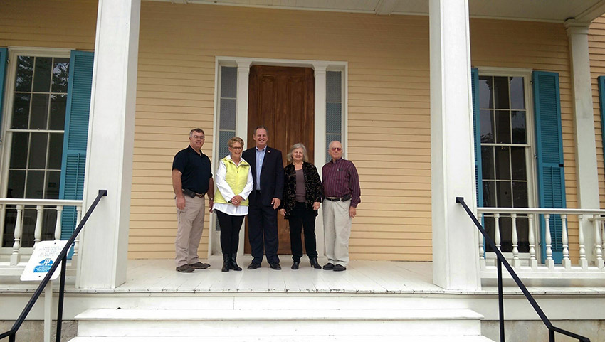 Three white men and two white women standing on covered porch at front door of multistory plantation house