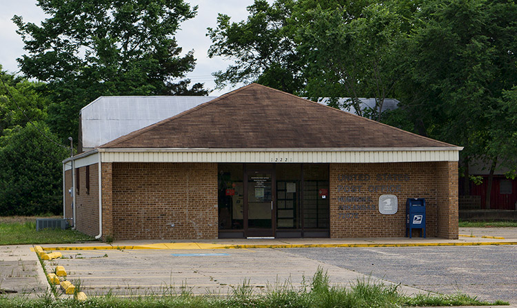 Single-story brick building on parking lot with blue mail box