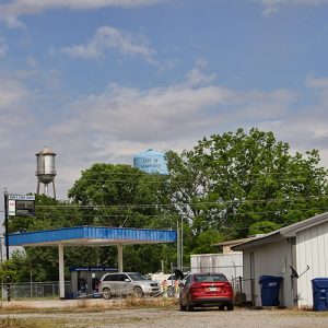 Service station wit blue canopy and buildings with two water towers in the background