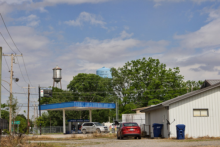 Service station wit blue canopy and buildings with two water towers in the background
