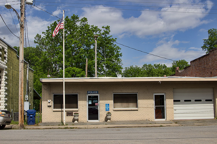 Single-story brick police building with garage bay door on street with flag pole