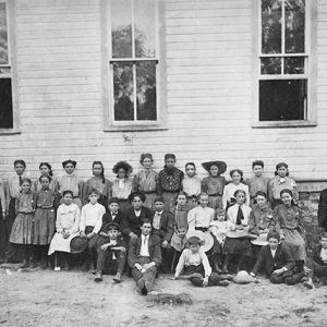 White children and teachers posing together outside building with wood siding and rectangular windows
