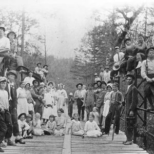 Group of white men women and children standing and sitting on steel bridge rails and platform